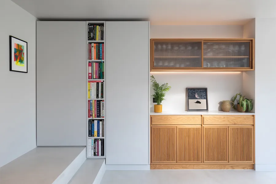 Grey tall units with a slim built-in bookcase beside the steps, next to the oak sideboard.