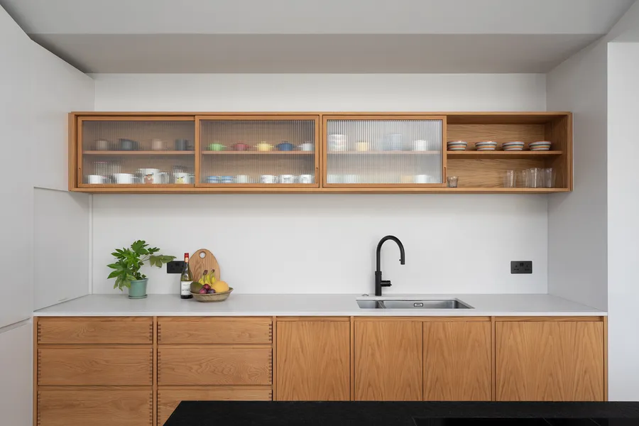 Sink run with oak drawers and doors, white worktop and oak wall unit with reeded glass.