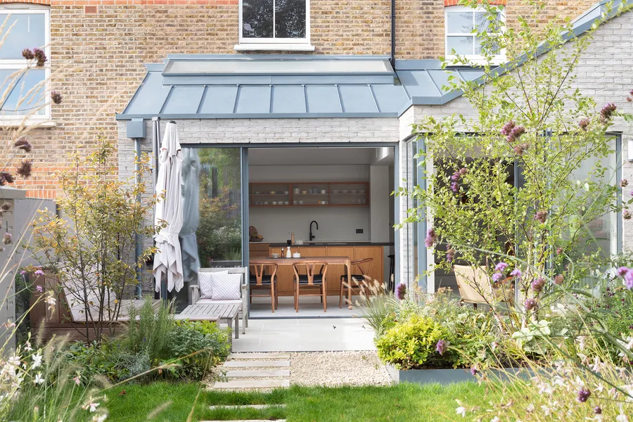 Oak island with black worktop and bar stools in the rooflit extension, garden doors beyond.