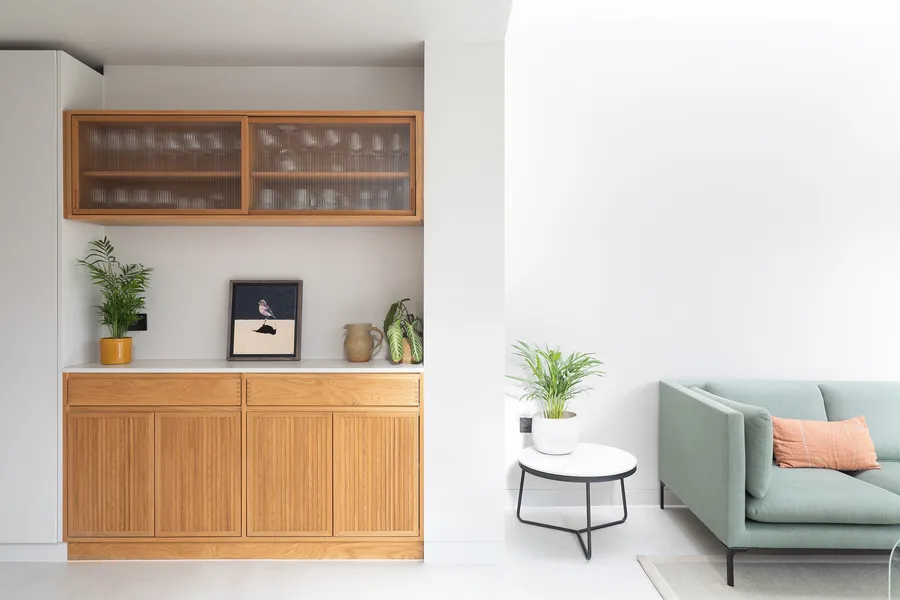 Oak sideboard with slatted doors and reeded glass wall unit beside the living area sofa.