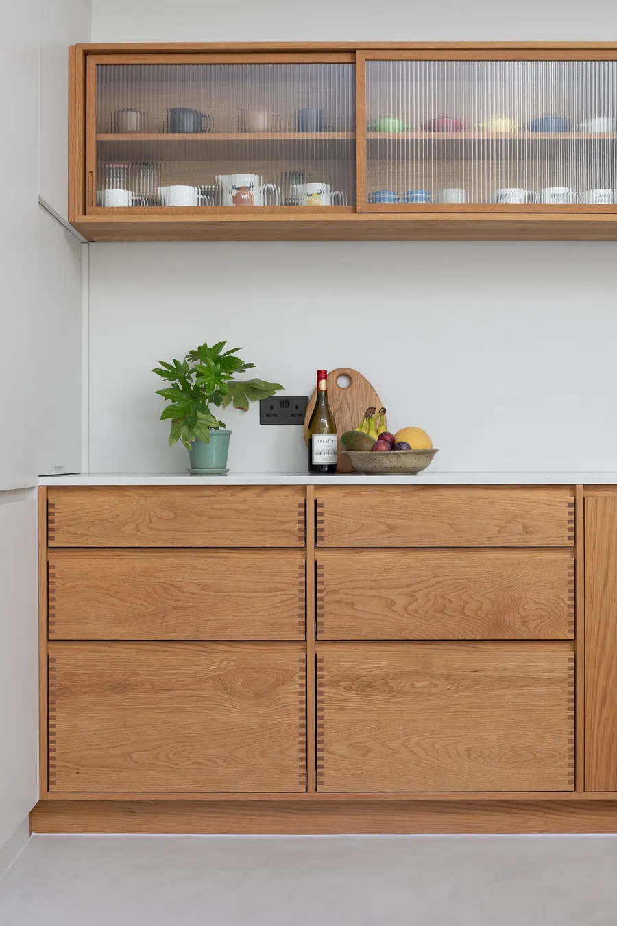 Finger-jointed solid oak drawer bank with white worktop and reeded glass wall unit above.