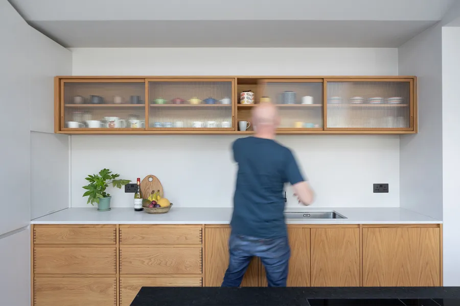 Person reaching into the oak and reeded glass wall unit above the kitchen sink run.