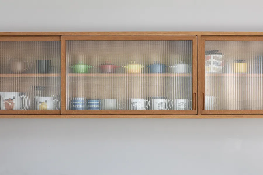 Close-up of the oak wall unit with sliding reeded glass doors, closed over mugs and pots.