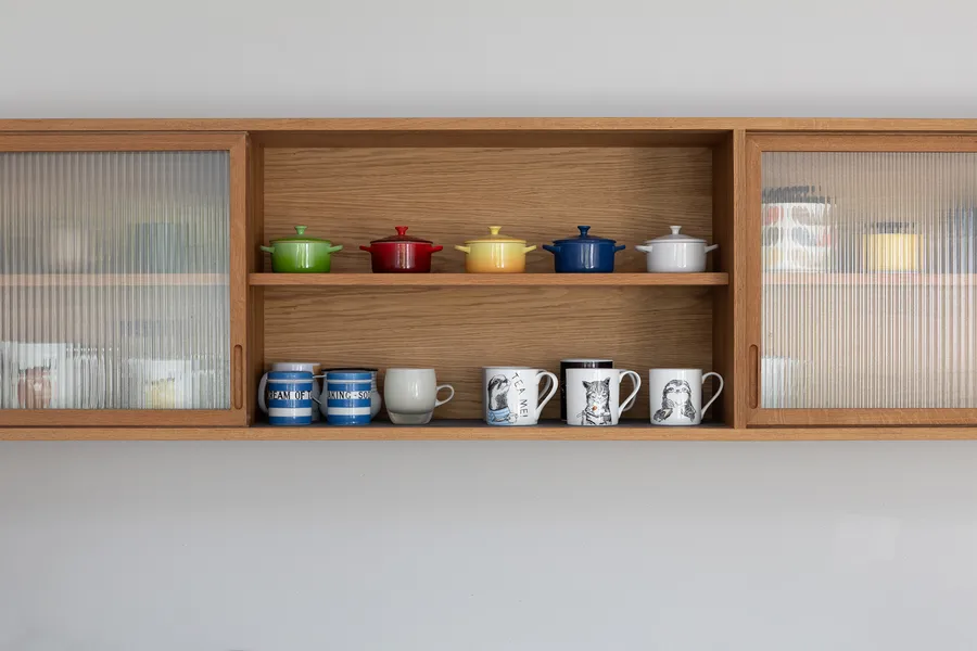 Oak wall unit with the centre bay open, showing a shelf of coloured pots above striped mugs.