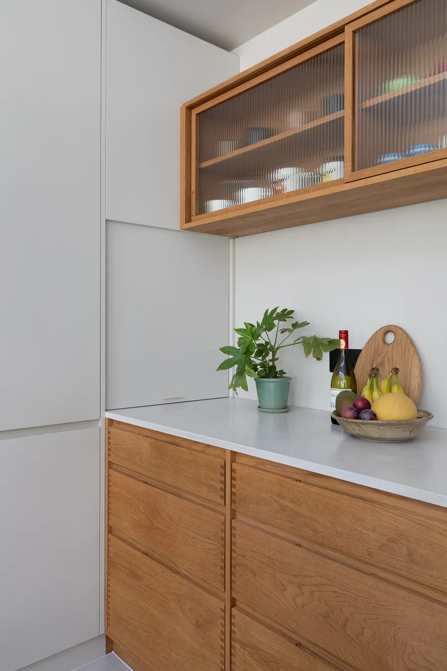 Appliance cupboard closed flush with the grey tall units above the white worktop and oak drawers.