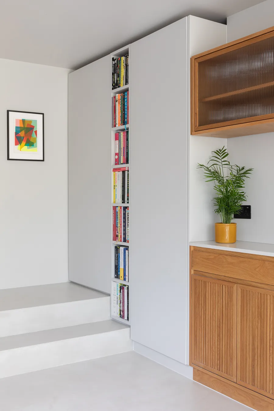 Tall grey cupboards with narrow open bookshelves built around the steps into the kitchen.