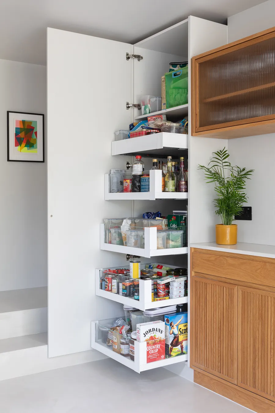 Tall larder cupboard open to show white pull-out drawers stocked with food and bottles.
