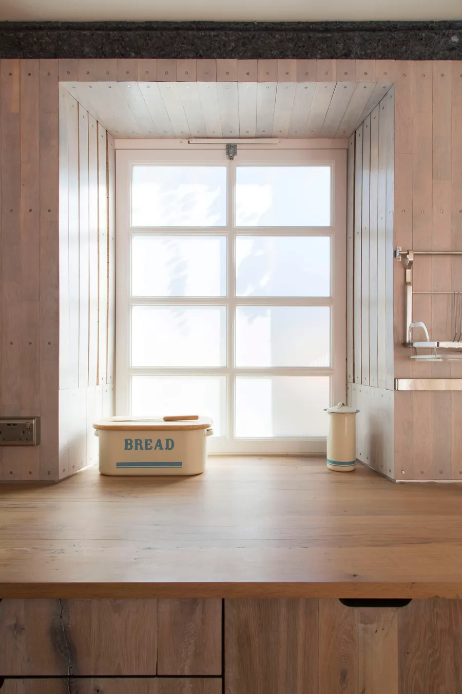 Reclaimed oak worktop beneath a deep window reveal lined with pale timber boards.