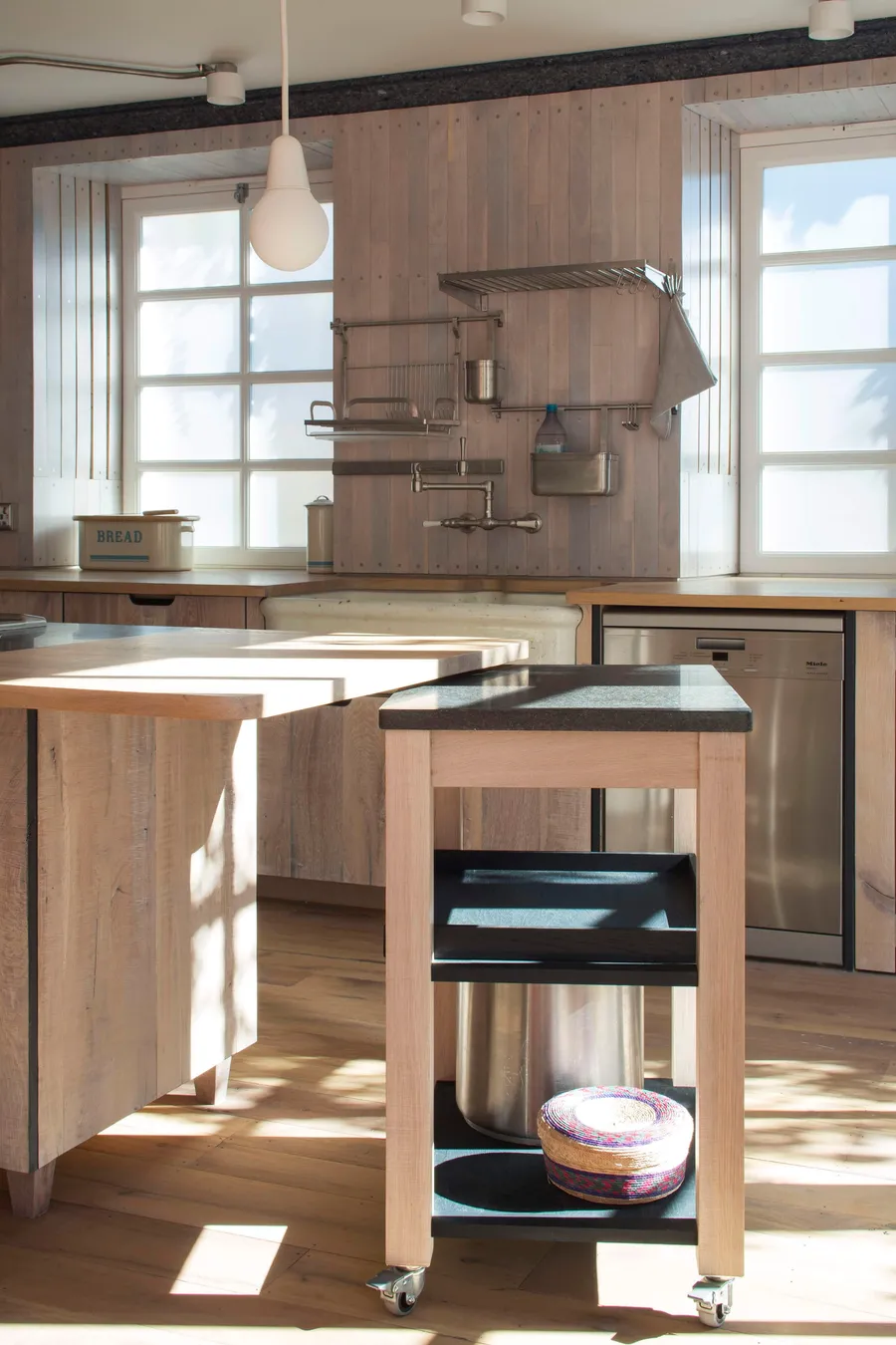 Oak trolley on castors beside the island, with wall-mounted steel racks above the butler sink.