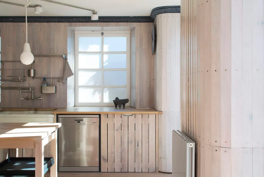 Curved timber-boarded corner and slatted oak cabinet doors beside an integrated dishwasher.