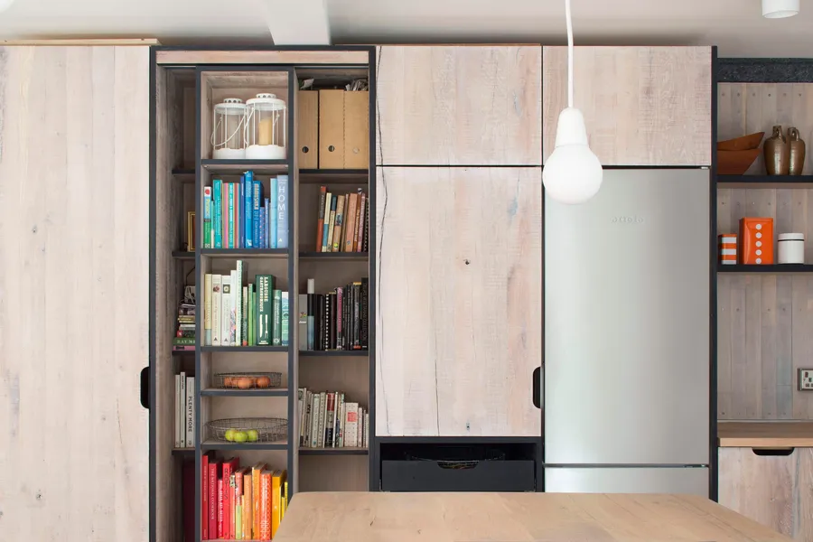 Sliding bookcase with dark steel frame between reclaimed oak tall cabinets and fridge.