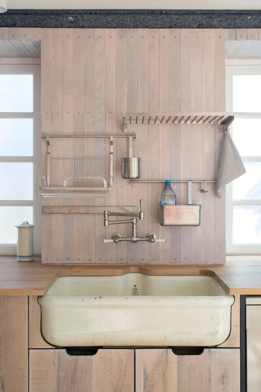Butler sink set into reclaimed oak worktop below a boarded splashback with steel racks and wall tap.