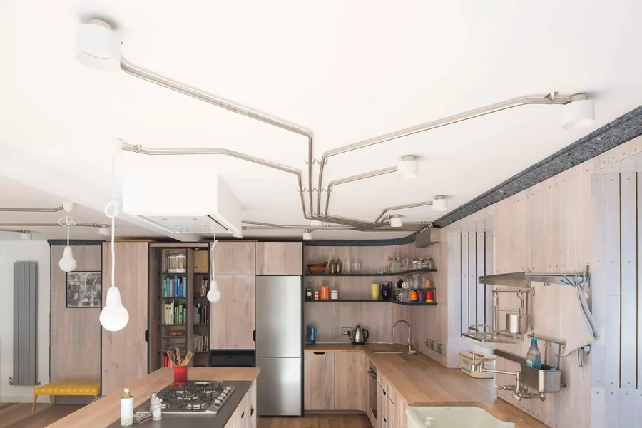 Exposed steel conduit lighting across the ceiling above the L-shaped reclaimed oak kitchen.