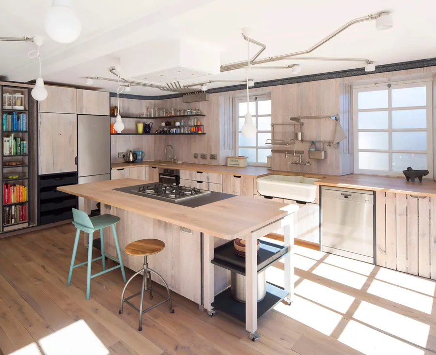 Reclaimed oak kitchen with island hob, butler sink, rolling trolley and sunlit timber floor.