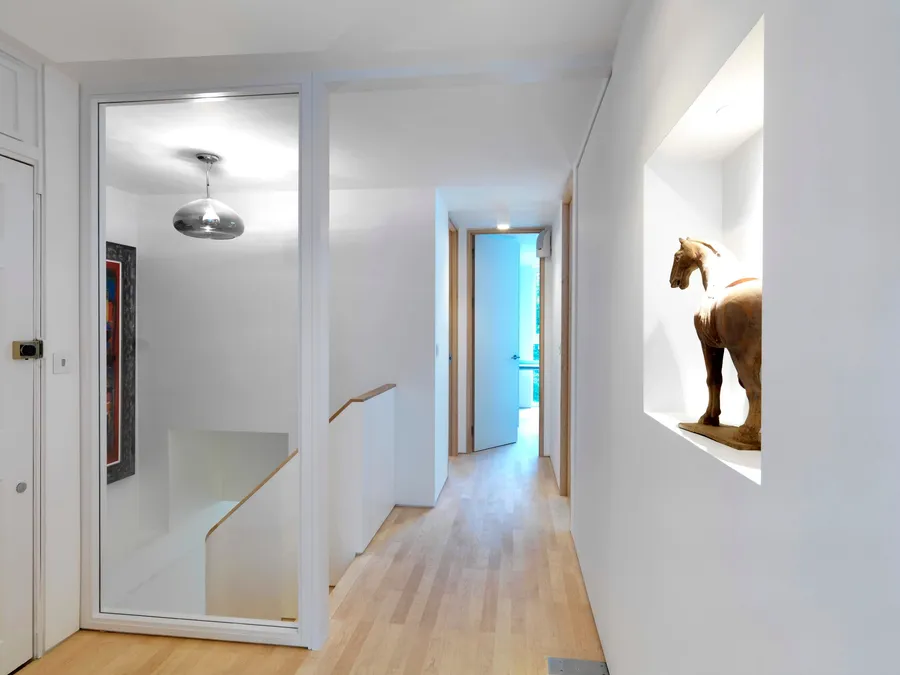 White landing with glazed stairwell screen, solid maple door frames and a sculpture niche.