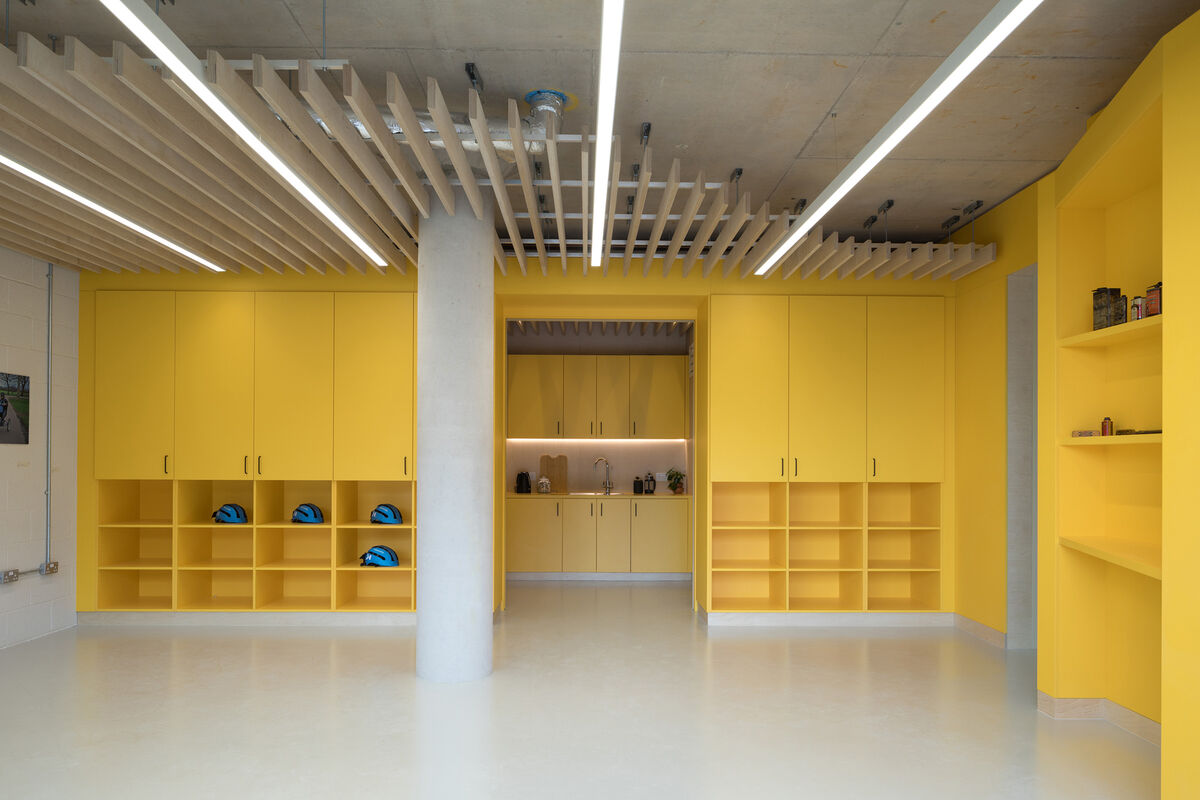 Bright yellow cabinetry, open shelving and a kitchenette fitted along the walls of the Bikeworks headquarters.