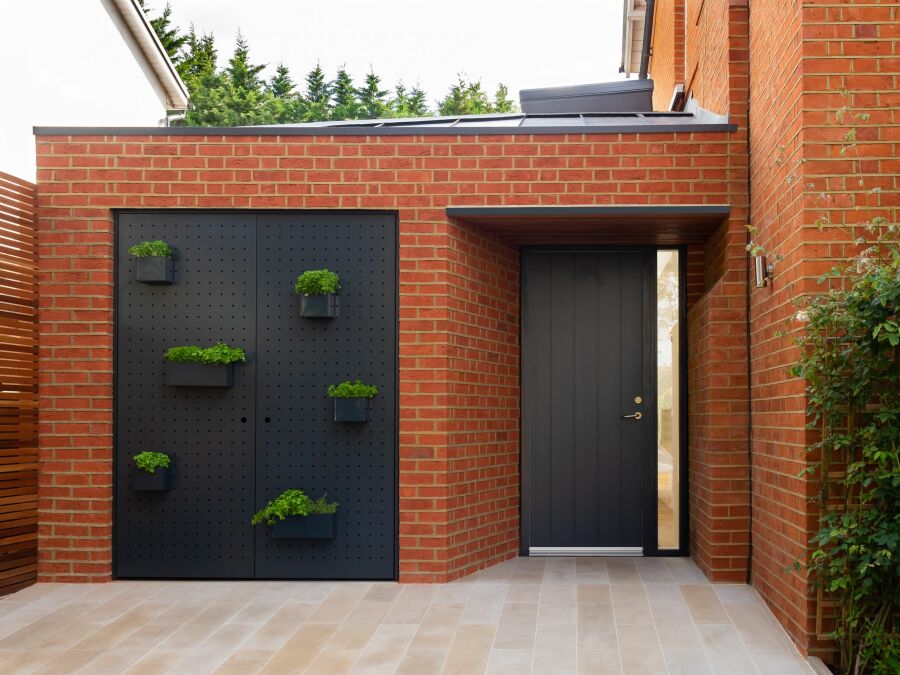 The external red brick frontage of modern extension, powder coated aluminum doors with moveable planters..
