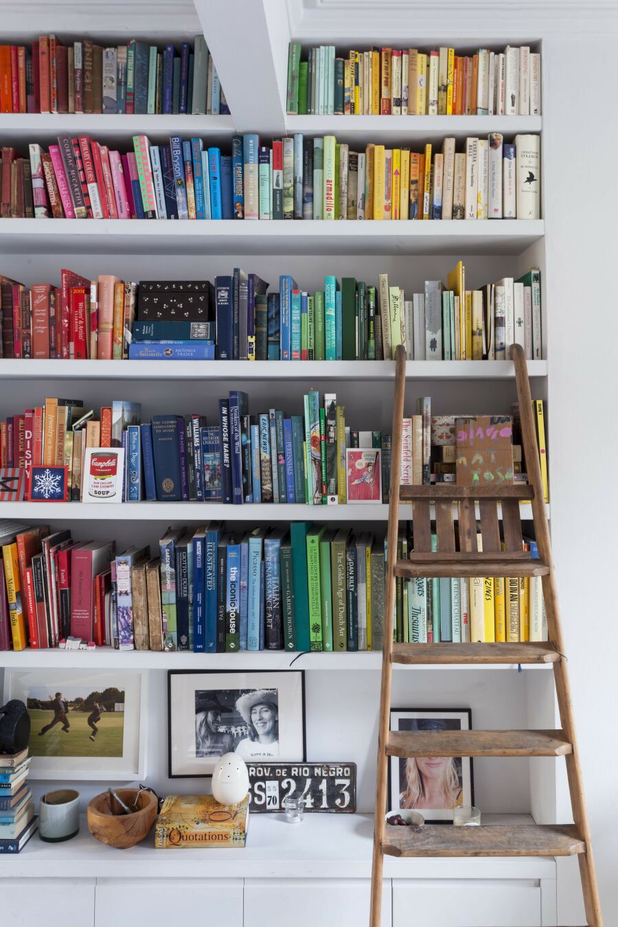 Colour coded books on floating ​library shelving with ladder steps..